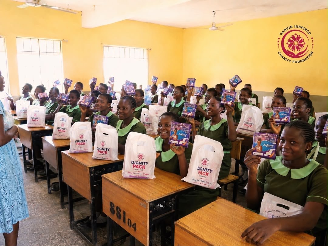 Schoolgirls in a classroom holding Dignity Pack hygiene kits from Garvin Inspired Charity Foundation